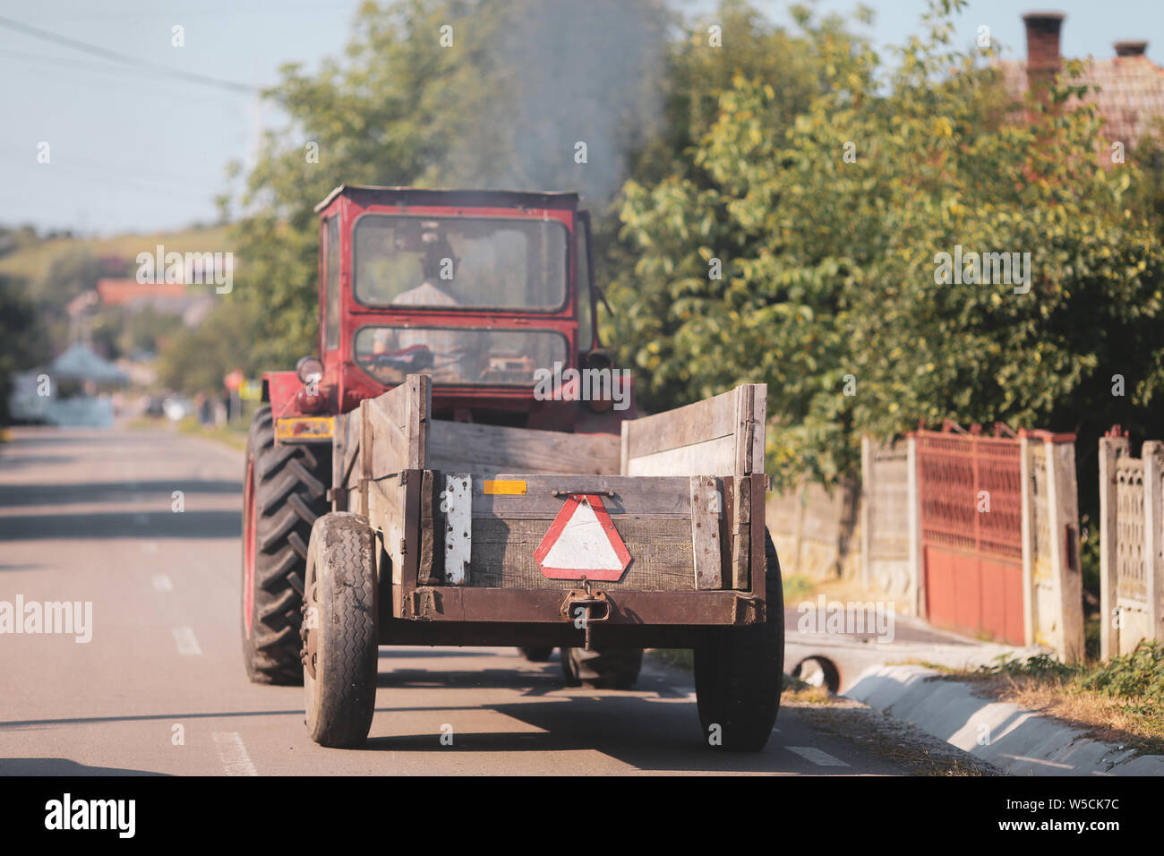 Vecchio trattore per le strade di un villaggio rurale in Romania con abbondante vegetazione attorno Foto Stock