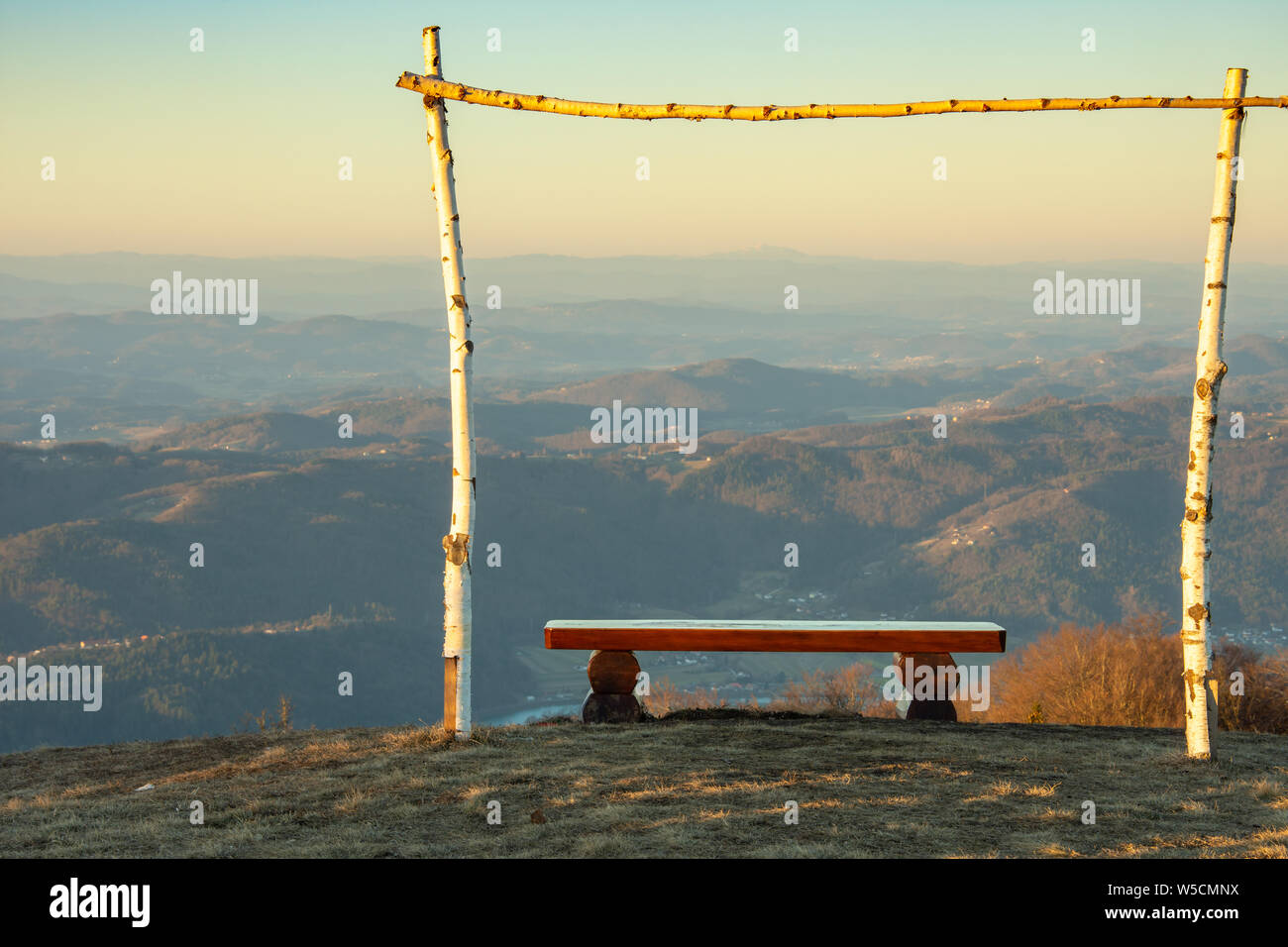 Panca in legno. Attorno ad esso è in legno a telaio di betulla. Il paesaggio della Slovenia al sunrise. La foto è stata scattata dalla cima della lisca hill Foto Stock