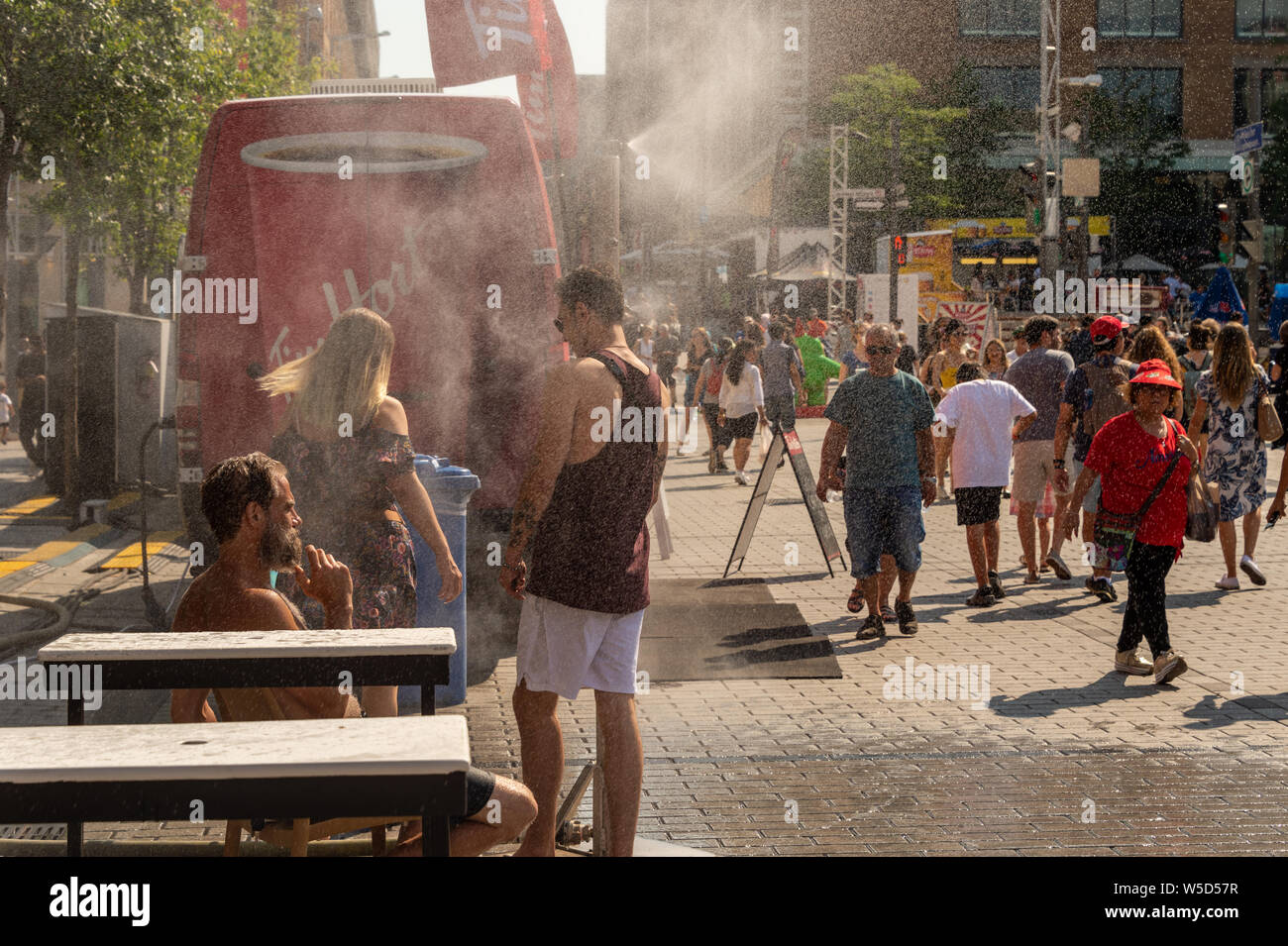 Montreal, CA - 27 Luglio 2019: la gente camminare sotto sistema di appannamento di raffreddarsi (nebbia sistema di raffreddamento) durante l'ondata di caldo nel Quartier des festivals. Foto Stock
