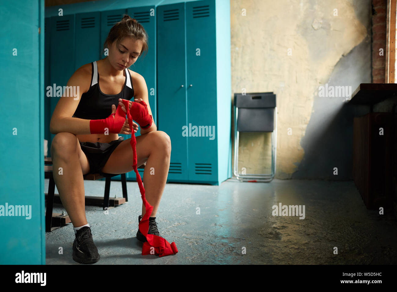 A piena lunghezza Ritratto di dura giovane donna mettendo in mano rossa si avvolge durante la preparazione per la boxe in pratica lo sport club, spazio di copia Foto Stock