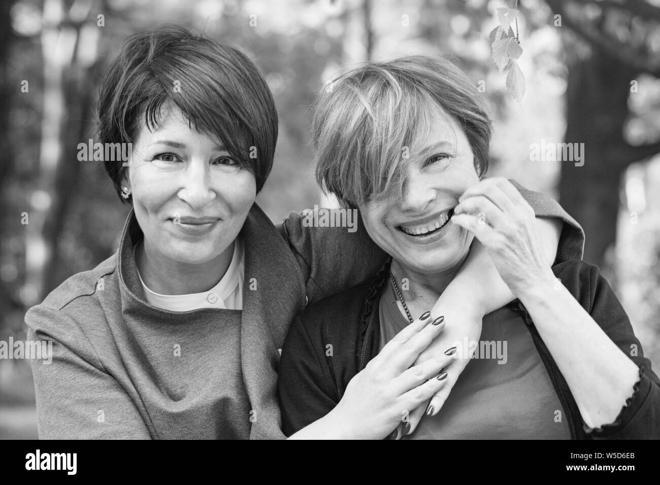 Due donne amici 60s e 40s anni abbracciando e passeggiate nel parco Foto Stock
