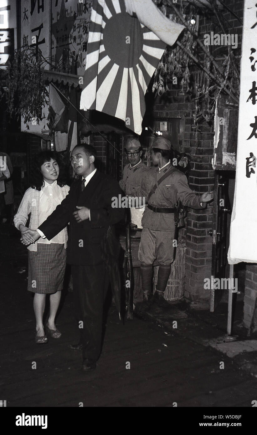 [ 1960 Giappone - Tokyo Night Club ] - Un lavoratore di ufficio e il suo compagno, più probabile una hostess, di fronte a una guerra themed night club in Tokyo, 1960 Showa (35). Foto Stock