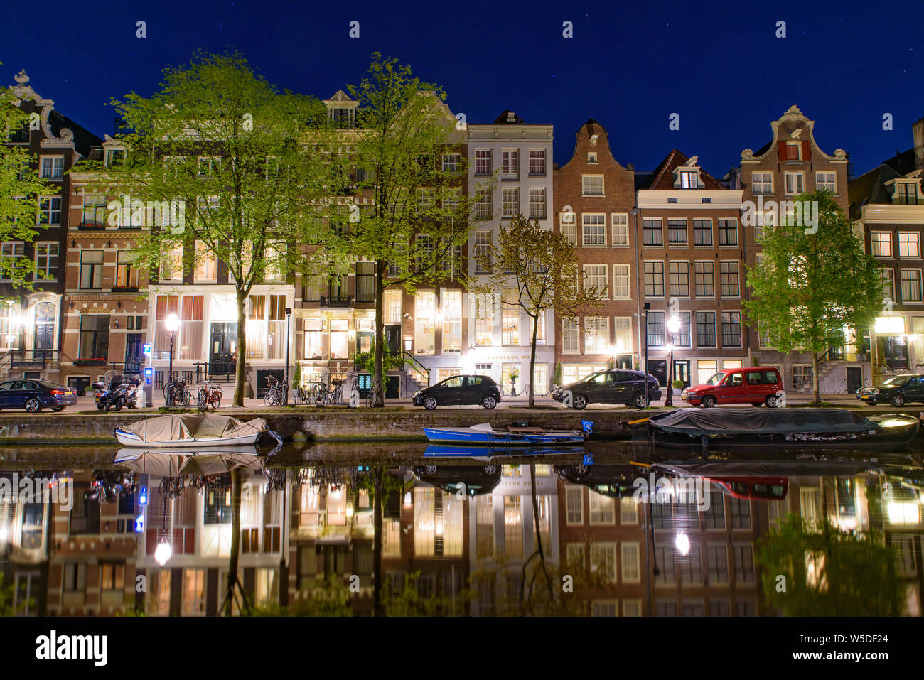 Vista notturna di edifici, alberi e barche lungo il canale di Amsterdam, Paesi Bassi Foto Stock