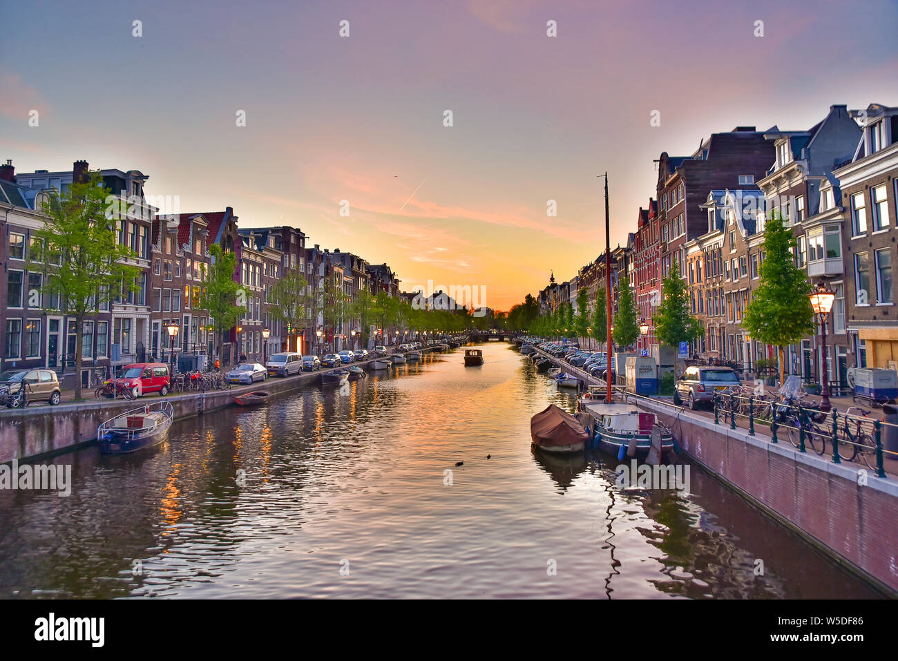 Edifici, alberi e barche lungo il canale al tramonto il tempo in Amsterdam, Paesi Bassi Foto Stock