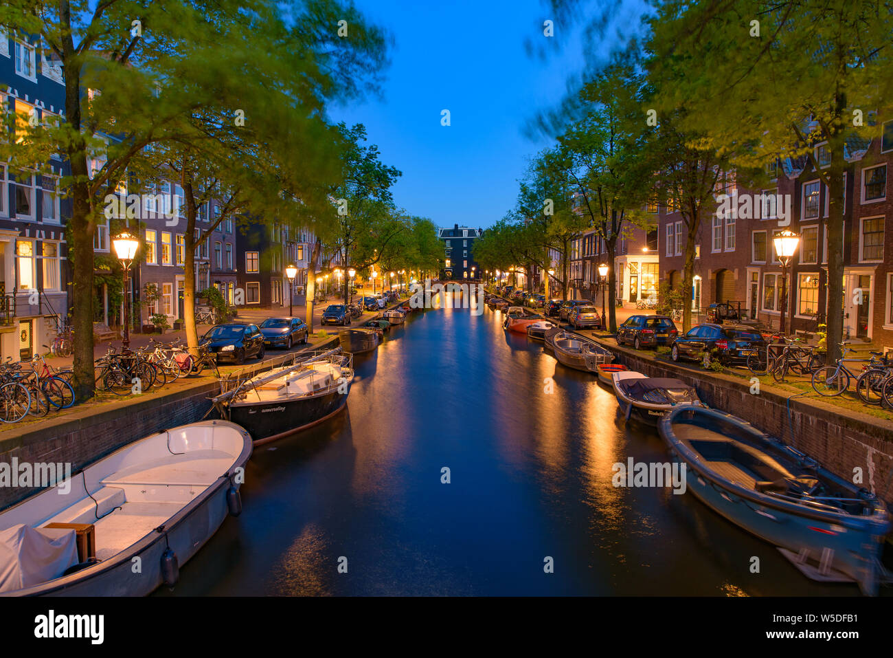 Vista notturna di edifici, alberi e barche lungo il canale di Amsterdam, Paesi Bassi Foto Stock