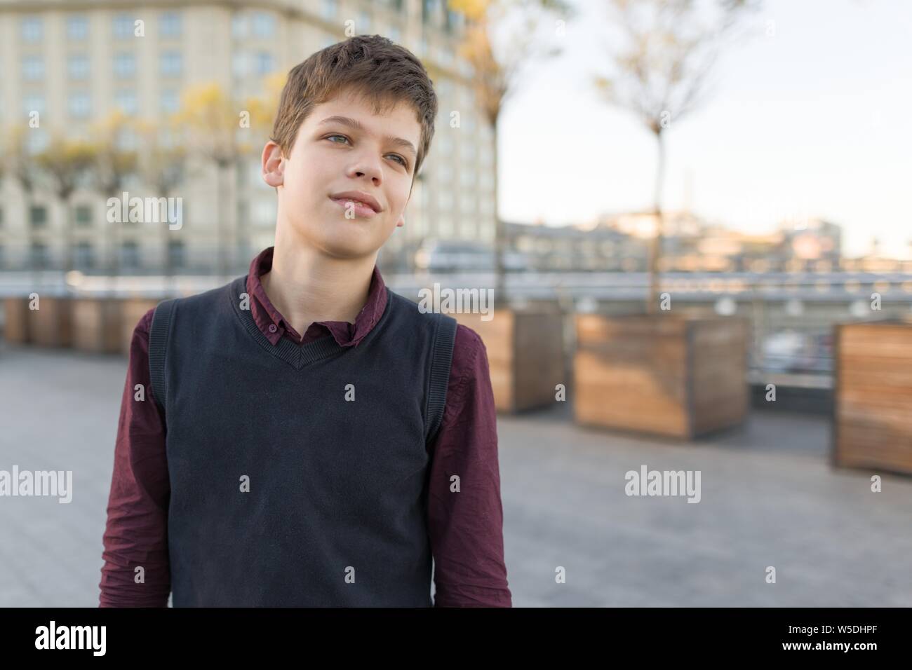 Outdoor ritratto di sorridente ragazzo adolescente 14, 15 anni. Sullo sfondo della città, ora d'oro, spazio di copia Foto Stock