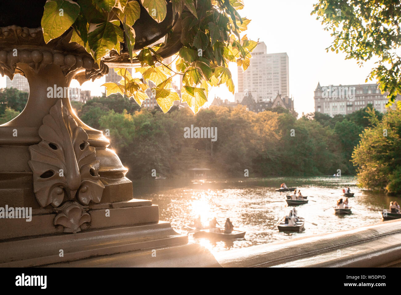 Estate a Central Park di New York City visto dallo storico ponte di prua con persone sconosciute nella riga barche nel lago. Foto Stock