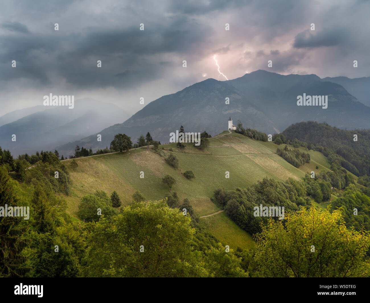 Grim paesaggio con telecomando chiesa sulla collina e la tempesta si avvicina attraverso montagne sullo sfondo Foto Stock