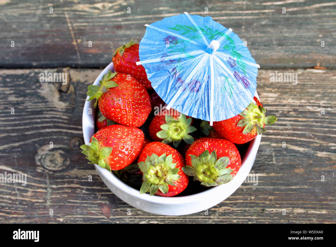 Una ciotola di fragole con una carta blu ombrello si siede su una tavola di legno a Gerusalemme in Israele. Foto Stock