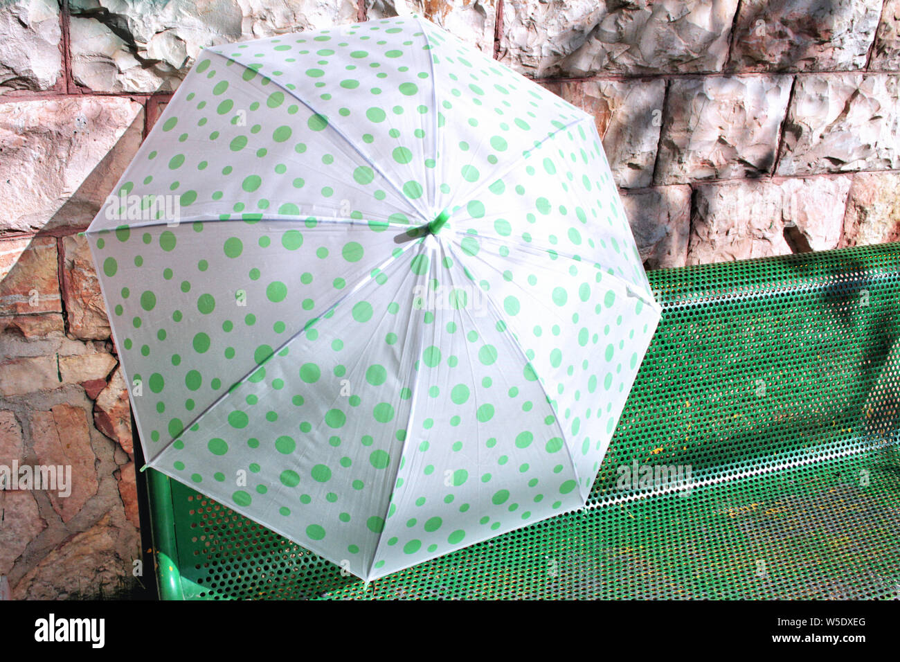 Un allegro verde e bianco polka dot ombrello aperto poggia su un banco verde contro un muro di pietra di Gerusalemme in Israele. Foto Stock