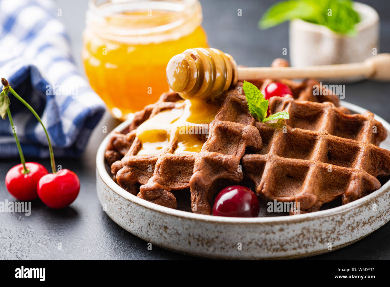 Tutto il grano cialde belghe con il miele e il ciliegio dolce sulla piastra, primo piano. Gustosi dessert o il cibo della colazione Foto Stock