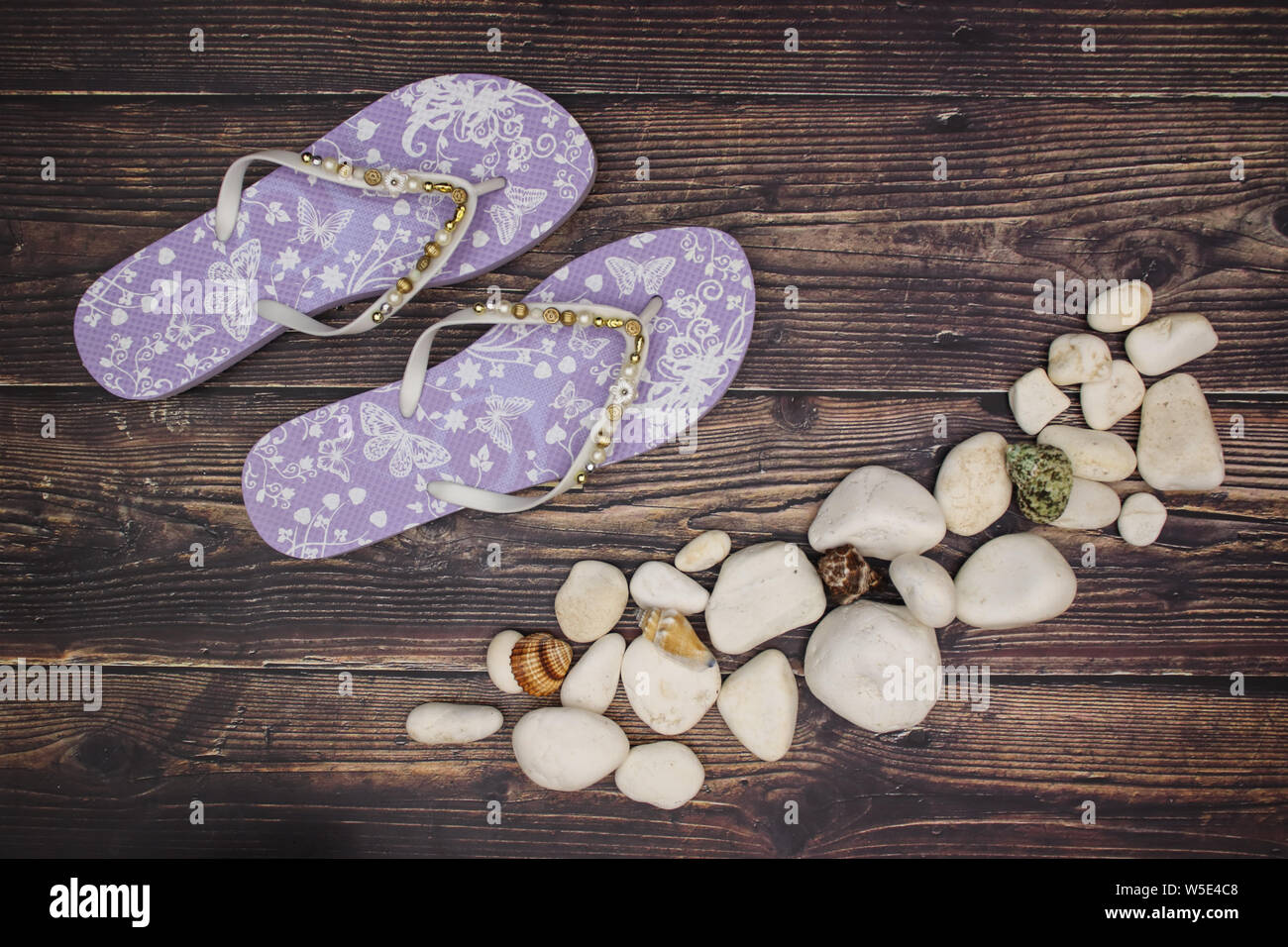 Rocce bianche e conchiglie con pantofole viola su sfondo di legno Foto Stock