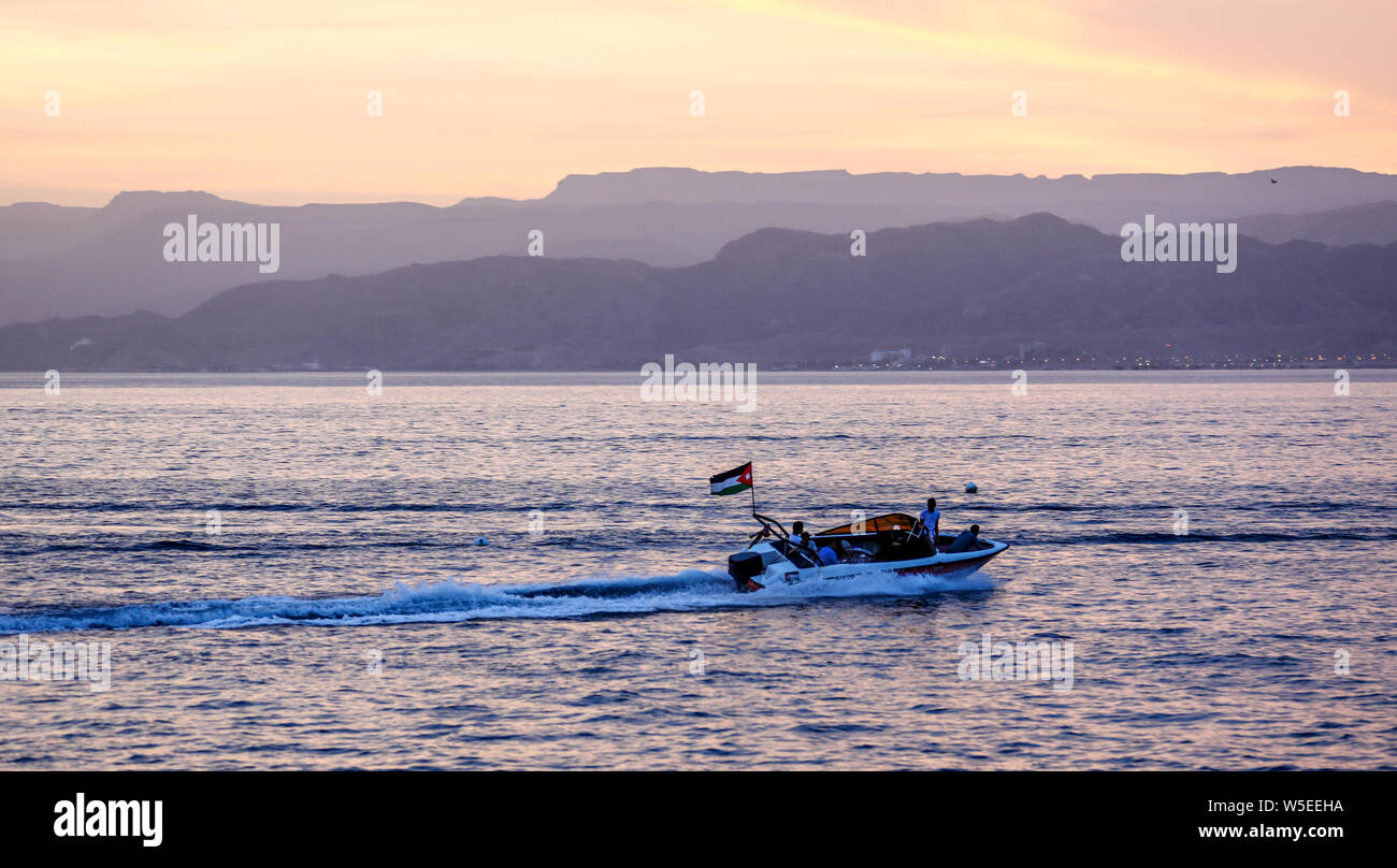 Stagliano quattro uomini in una barca veloce in Mar Rosso di Giordania passando da con un flag di giordani al tramonto. Foto Stock