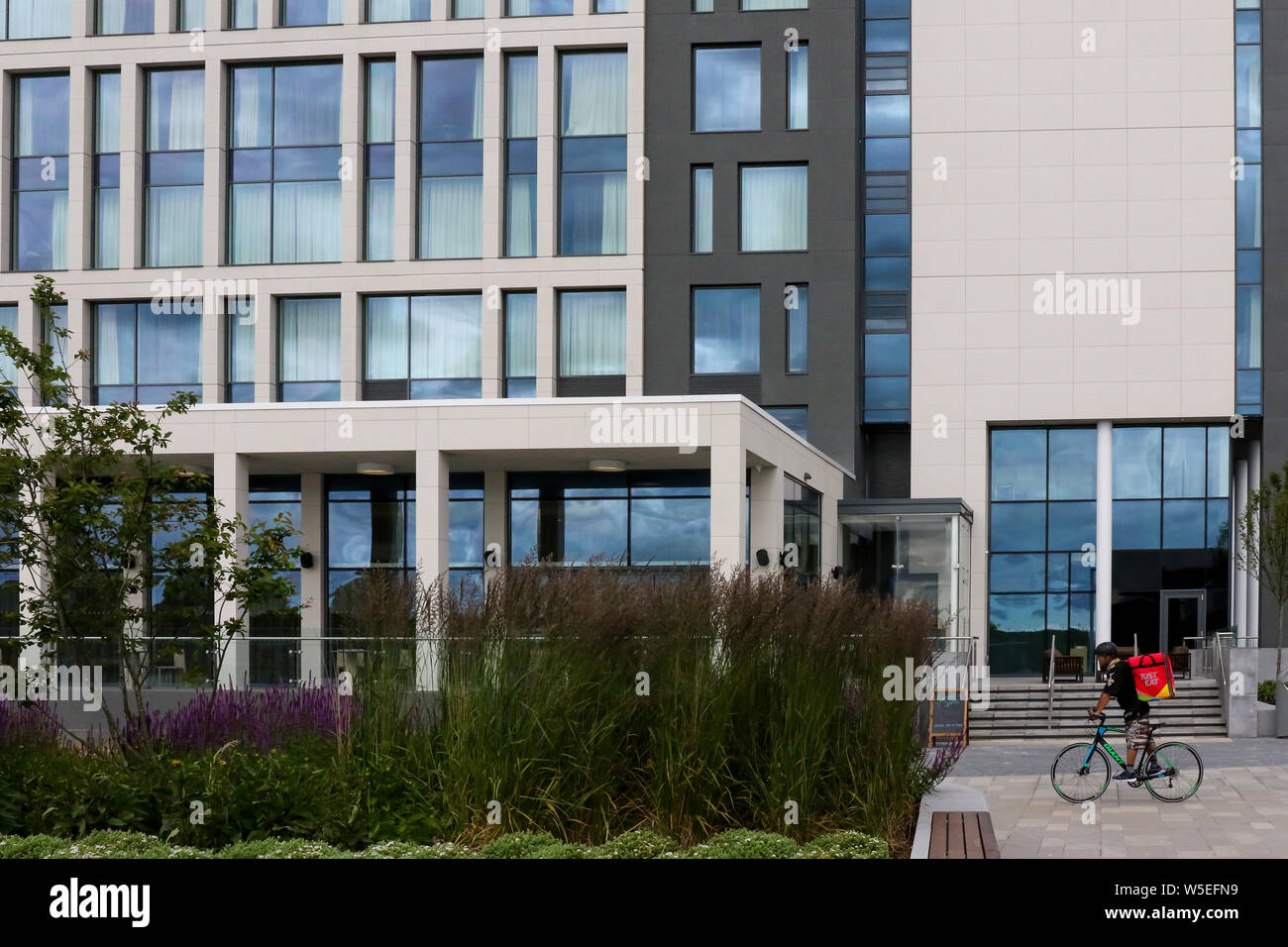 Solo mangiare ciclista con la sacca di erogazione passando davanti all'hotel a Belfast su una mattina d'estate. Foto Stock