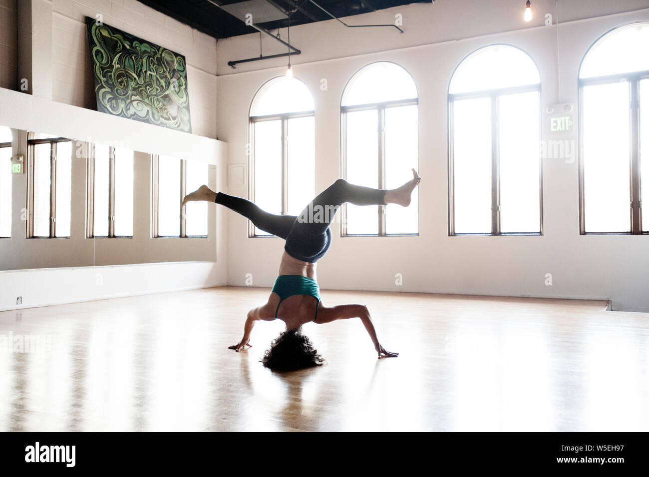 La donna a praticare yoga in uno straordinario headstand con una torsione. Una splendida finestra luce in un vecchio studio di danza. Foto Stock