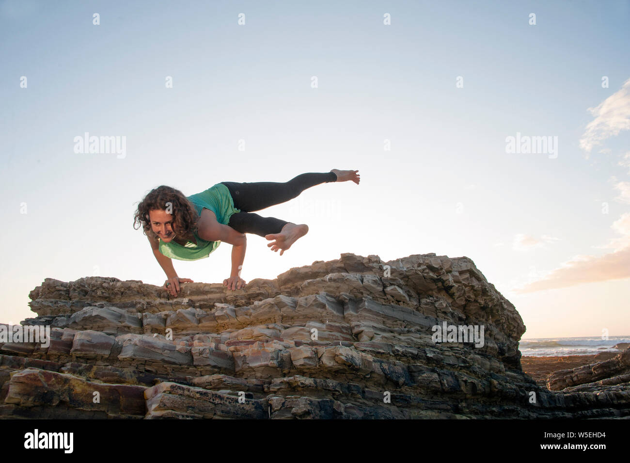 Donna felice equilibrio di yoga su pietra dal mare. Bella giornata in ritardo i colori. Foto Stock