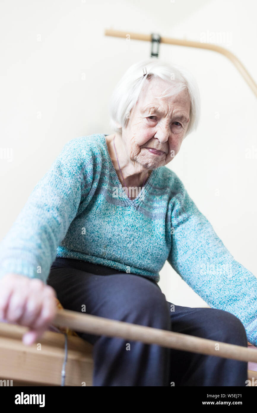 Anziani 96 anni vecchia donna esercizio con un bastone seduta sul suo cattivo. Foto Stock