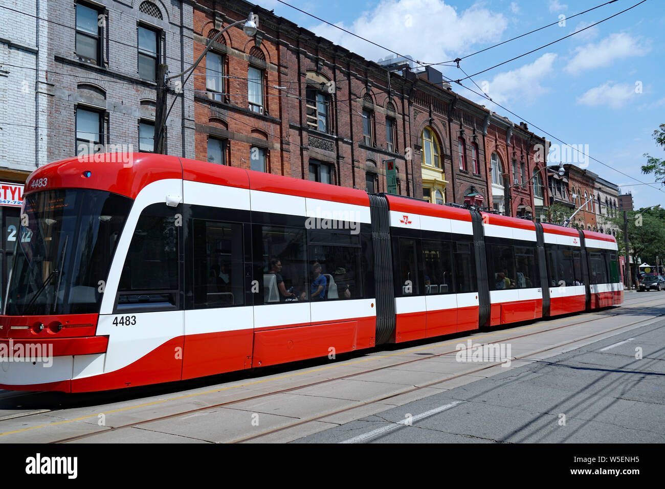 TORONTO - Luglio 2019: un lungo moderno tram di articolazione va passato Vittoriano di vecchi edifici commerciali su Queen Street. Foto Stock