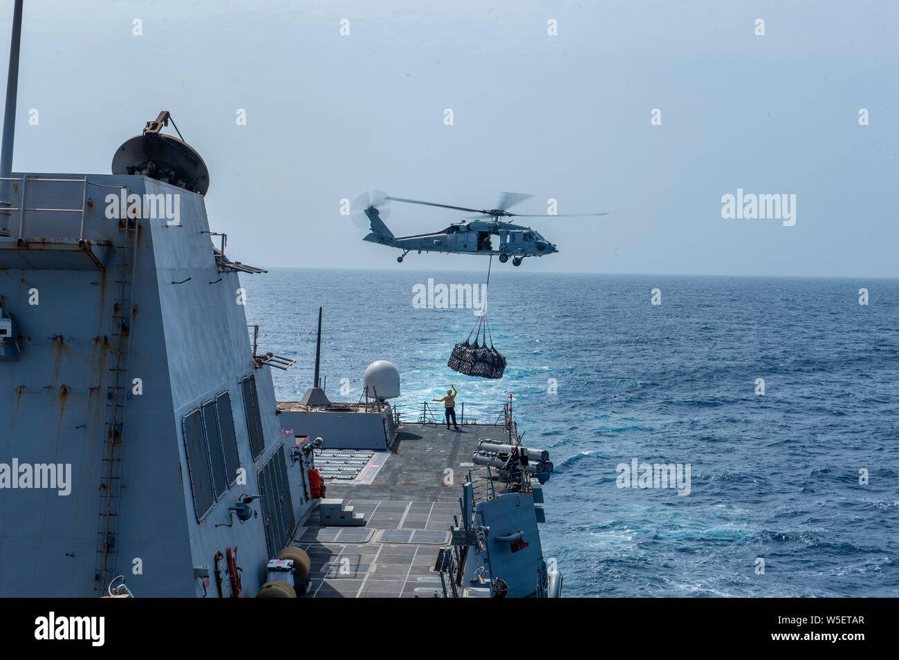 190724-N-SS350-1058 Mar Arabico (24 luglio 2019) un MH-60S Sea Hawk elicottero, assegnato al "Nightdippers" di elicottero di mare squadrone di combattimento (HSC) 5, offre negozi per il Arleigh Burke-class guidato-missile destroyer USS Bainbridge (DDG 96) durante un rifornimento in mare. Bainbridge è distribuito negli Stati Uniti Quinta Flotta area di operazione a sostegno di operazioni navali per garantire stabilità marittimo e la sicurezza nella regione centrale, collegando i paesi del Mediterraneo e del Pacifico attraverso l'Oceano Indiano occidentale e tre strategici punti di strozzatura. (U.S. Foto di Marina di Massa Specialista comunicazione 3° Cla Foto Stock