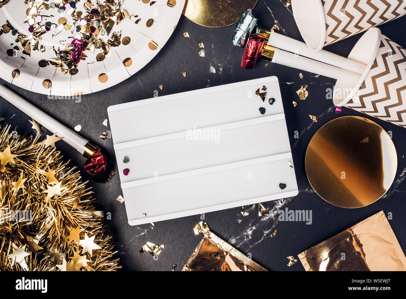 Felice anno nuovo partito con il fustellato scatola luminosa con party cup,parte soffiante,tinsel,coriandoli.divertente festeggiare holiday party time table top view.banner mock up b Foto Stock