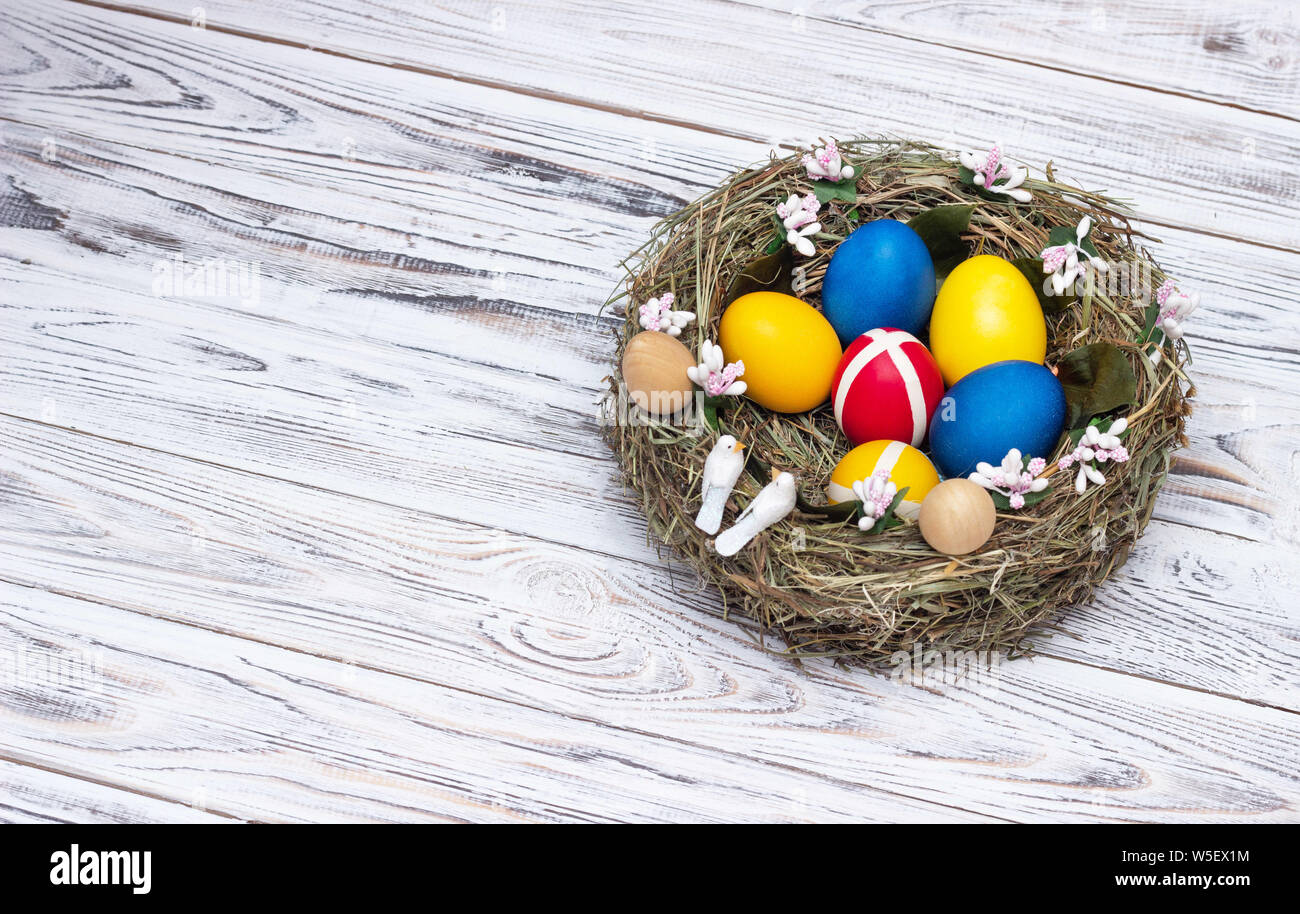 Nido con multi-colore di uova di pollo su un bianco sullo sfondo di legno, il concetto di custom e il rituale del festival di Pasqua e la comparsa di SPR Foto Stock