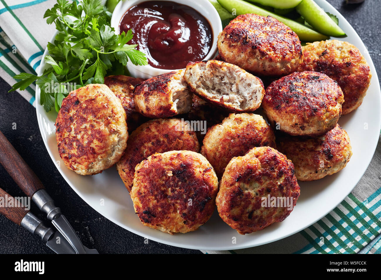 Close-up di polacco polpette di carne serviti con fette di cetriolo e salsa barbecue su una piastra bianca su una tabella di calcestruzzo con fette di baguette francese, hori Foto Stock