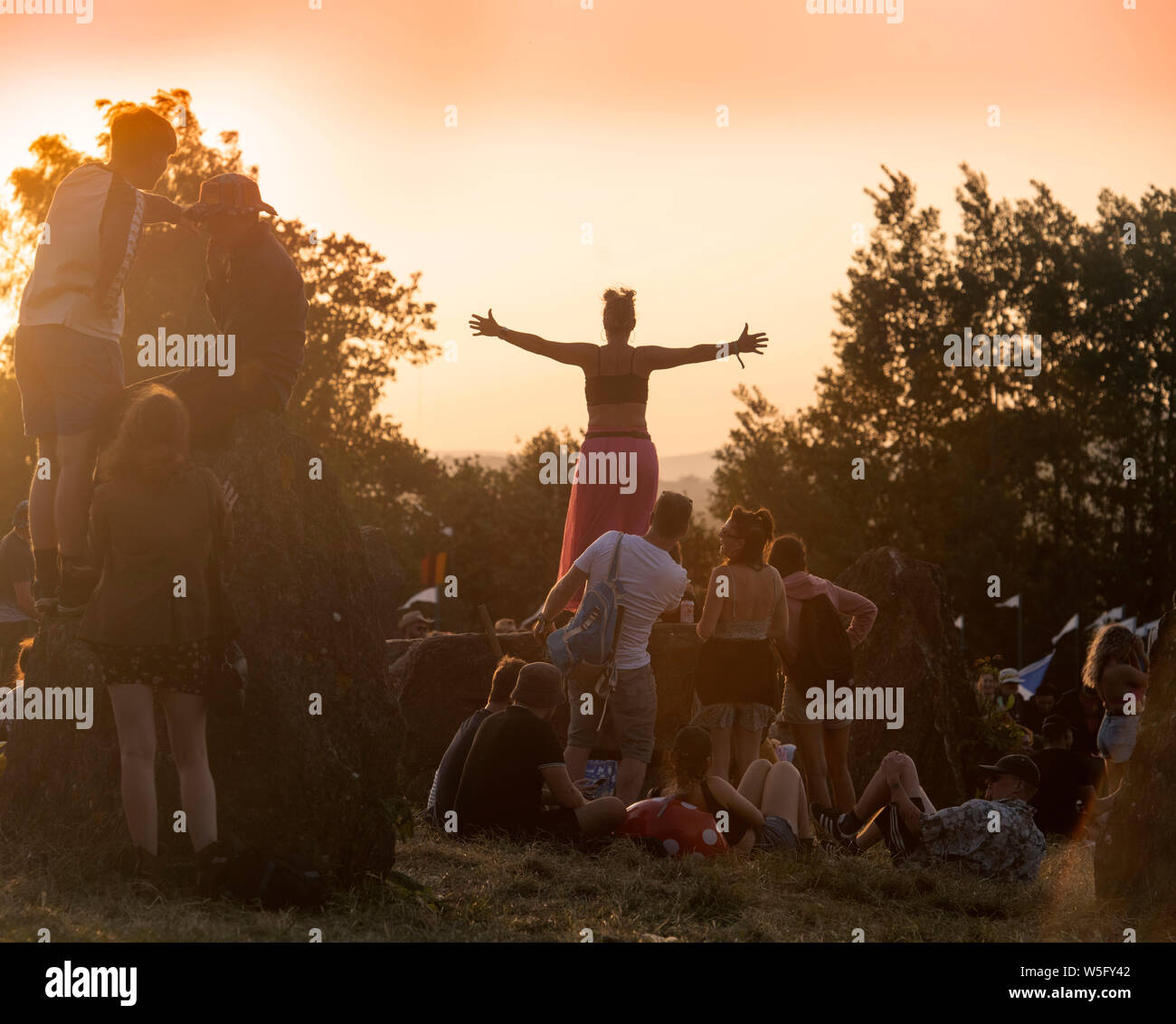 La folla al cerchio di pietra come il sole tramonta al Glastonbury festival 2019 in Pilton, Somerset Foto Stock