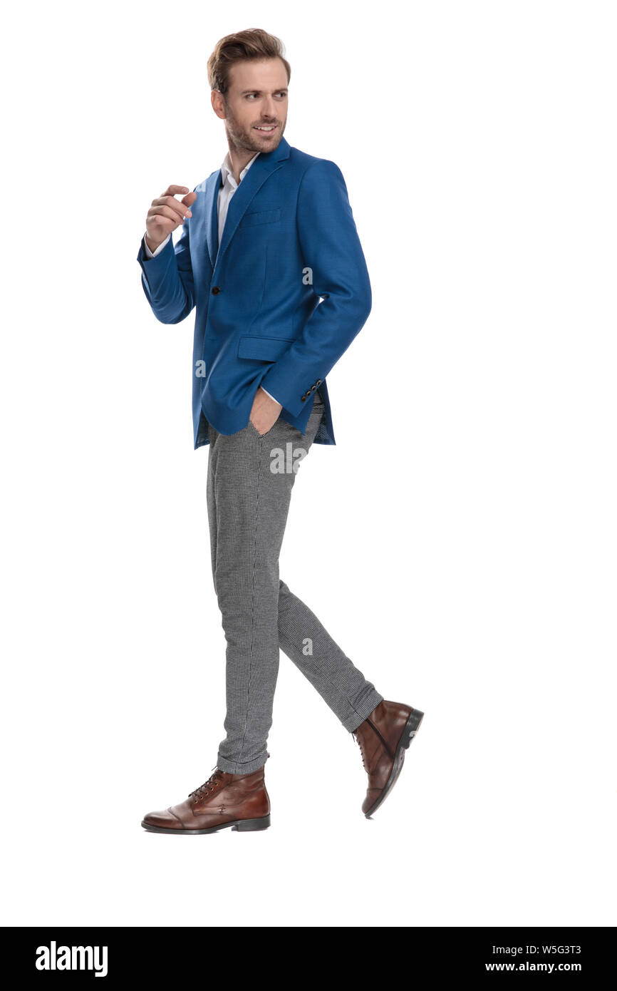 Vista laterale di un unpleased uomo informale tenendo la mano in tasca e a piedi mentre indossa una tuta bianca su sfondo per studio Foto Stock