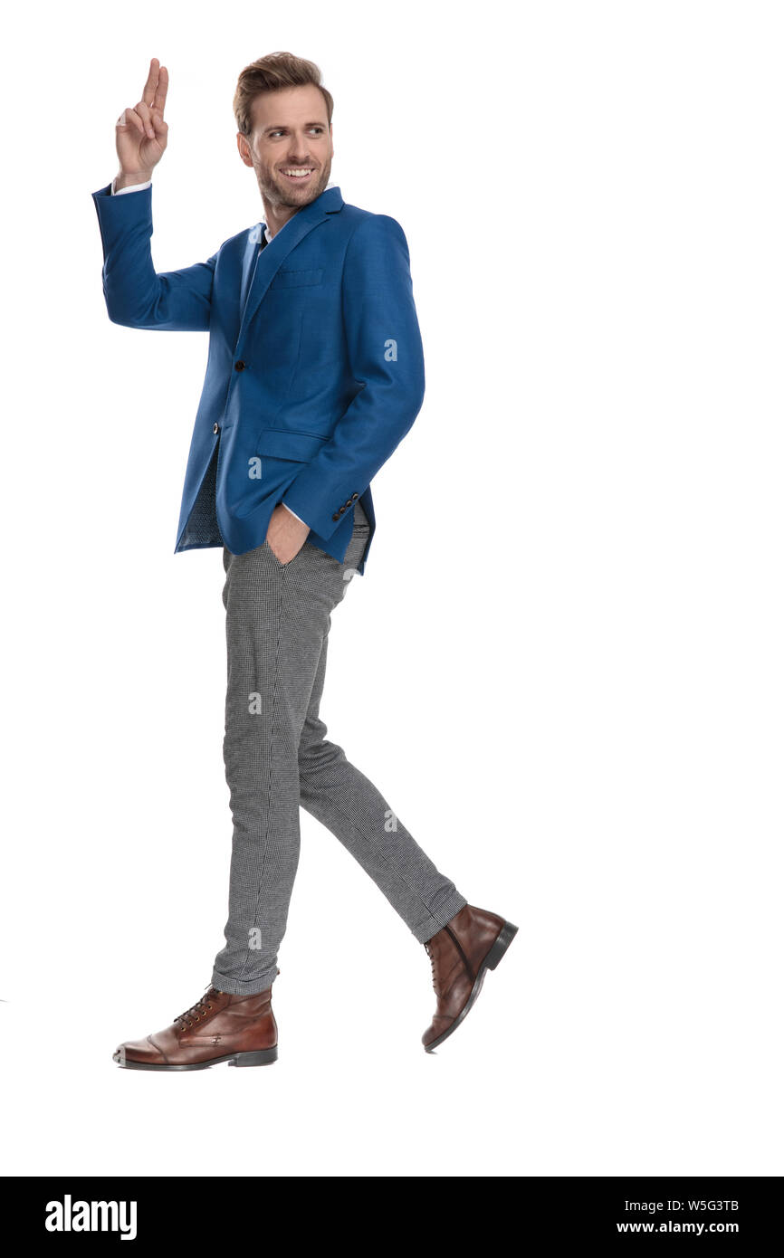 Vista laterale di attraenti uomini casual saluto con la mano in tasca mentre fai un passo e indossando un abito elegante di colore bianco su sfondo per studio Foto Stock