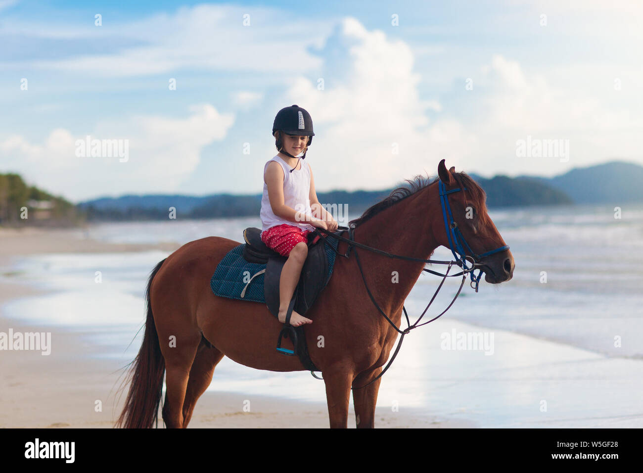 I bambini a cavallo sulla spiaggia. Bambini corsa dei cavalli. Carino bambina su pony su un ranch. Bambino e animale. Capretto nel casco sicuro per cavallo di classe. Trave Foto Stock