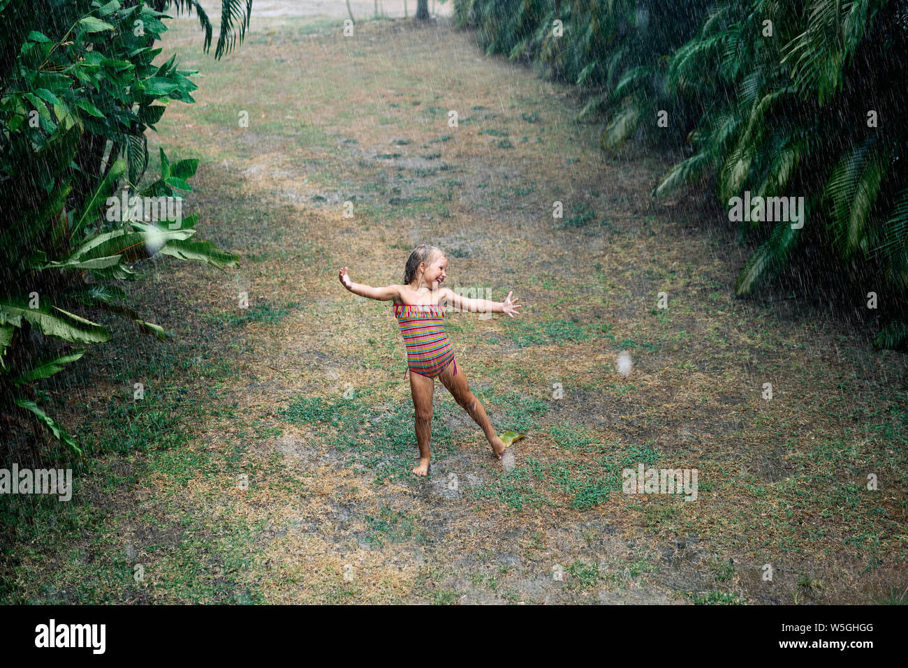 Graziosa bambina godere la pioggia e balli sulla strada sotto la pioggia in estate. I bambini e la Felicità, gioia e piacere Foto Stock