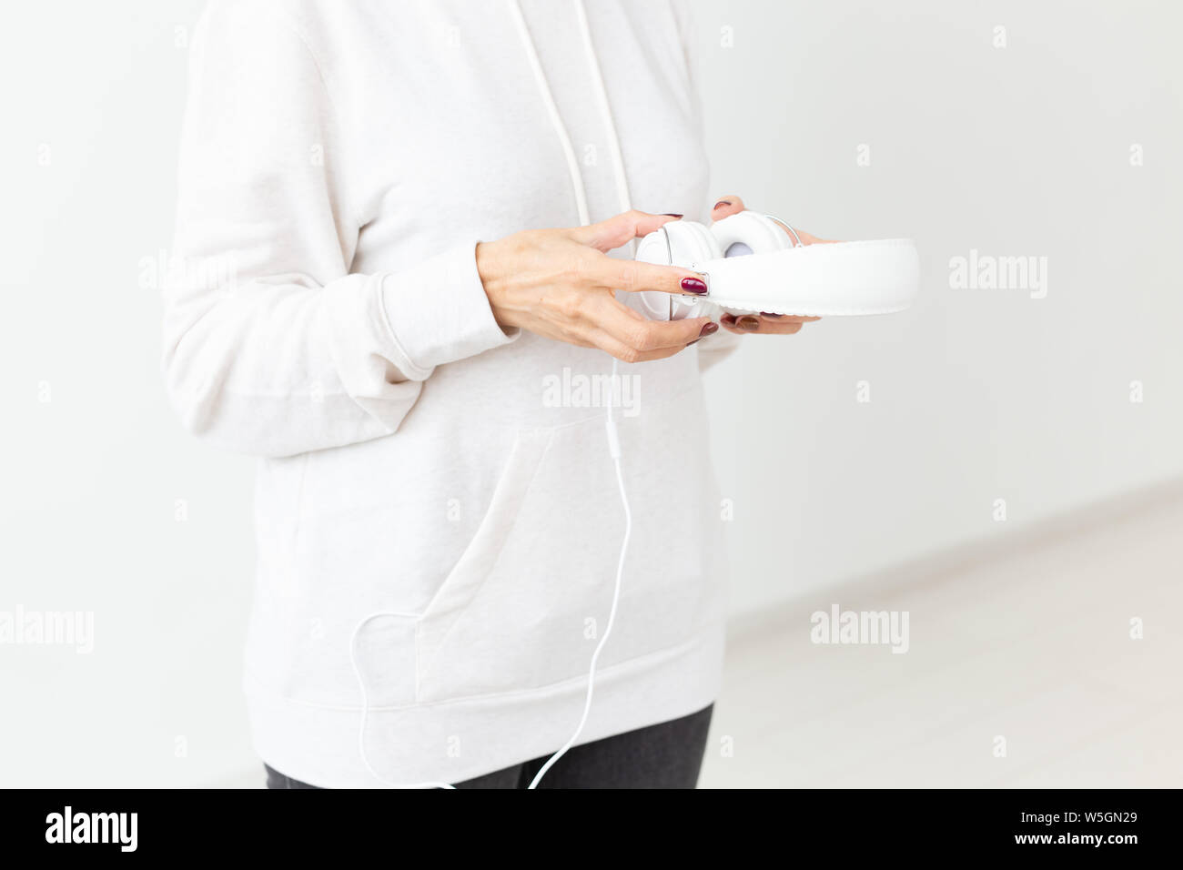 Close-up di donna indefinita in felpa con cuffie tenuta in piedi su uno sfondo bianco. Concetto di hobby e abbonamenti a radio preferiti stat Foto Stock