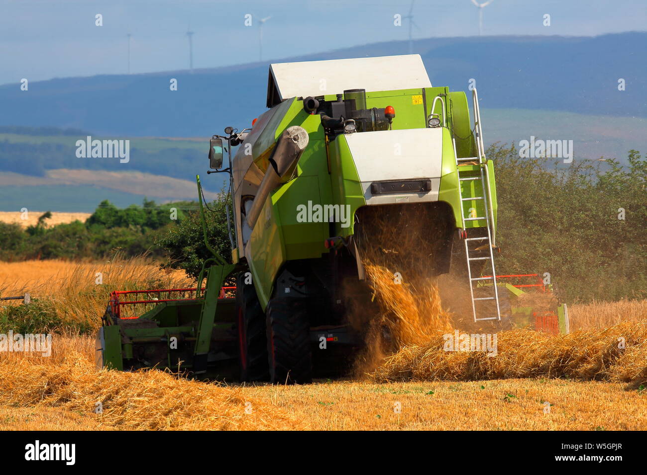 Una Mietitrebbia Harvester Works modo esso intorno ad un piccolo campo di campagna la raccolta di questi anni il raccolto di grano rendendo il lavoro a breve di questo anni raccolto. Foto Stock