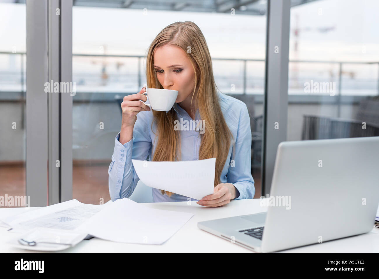 Giovane imprenditrice facendo di documenti e di bere il caffè in ufficio Foto Stock