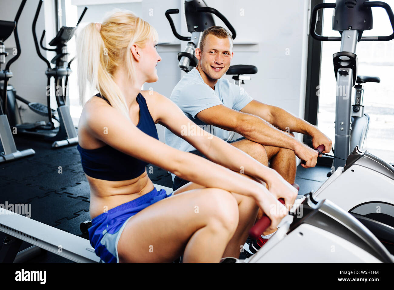 Giovane donna esercizio con un personal trainer su una macchina di riga Foto Stock