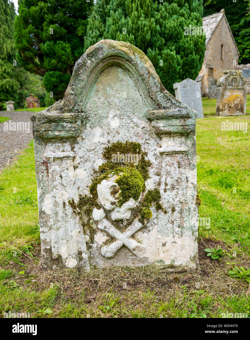 Cranio vecchio e ossa logorate sulla tomba nel cimitero, la chiesa parrocchiale di Humbie, Lothian orientale, Scozia, Regno Unito Foto Stock