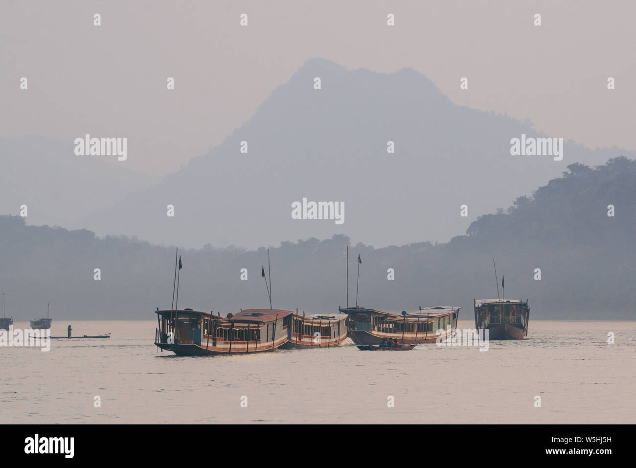 Tradizionale laotiana lento in legno barche sul fiume Mekong vicino a Luang Prabang al tramonto, Laos. Mountain sullo sfondo Foto Stock