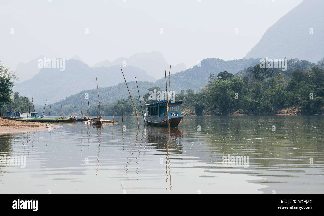 Tradizionale in legno laotiane barca lenta su Nam Ou fiume nei pressi di Nong Khiaw village, Laos. La riflessione in acqua Foto Stock