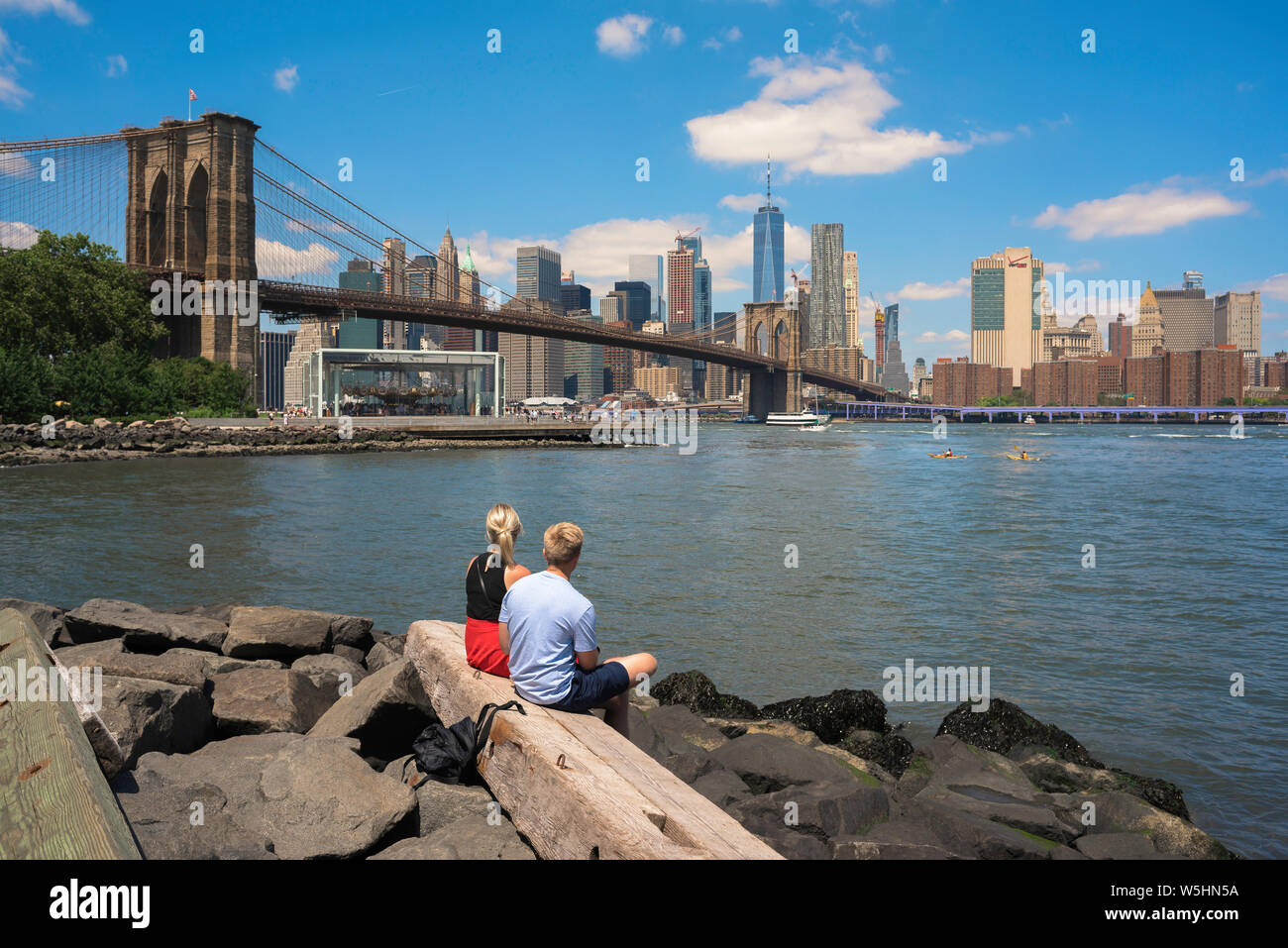 New York cityscape, vista del Ponte di Brooklyn e la parte inferiore dello skyline di Manhattan da Pebble Beach Park con due giovani situato nel primo piano, STATI UNITI D'AMERICA. Foto Stock