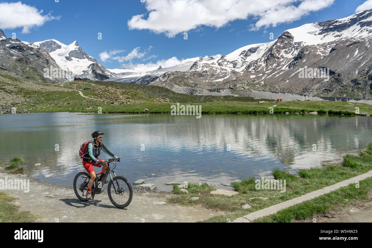 Attiva donna senior, cavalcando la sua mountainbike elettrico sotto il famoso Gornergrat in Zermatt, in background e Rimpfischhorn Strahlhorn,Wallis,sw Foto Stock