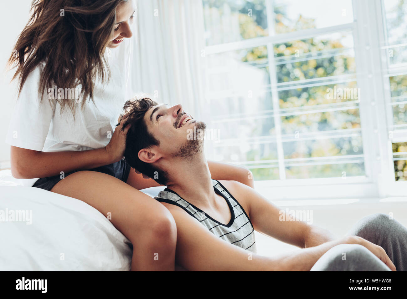 Giovane donna dando massaggio della testa per il suo fidanzato in camera da letto. Giovane rilassante insieme in camera da letto. Foto Stock