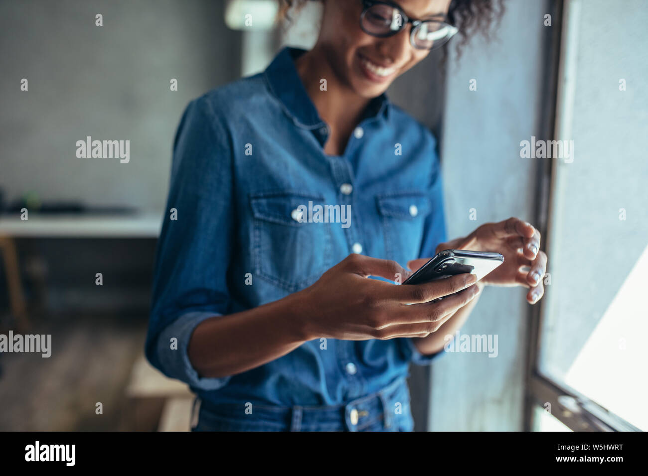 Imprenditore femmina in piedi in ufficio e utilizzando smart phone. Focus sul telefono cellulare in mano a una donna che indossa casuals. Foto Stock