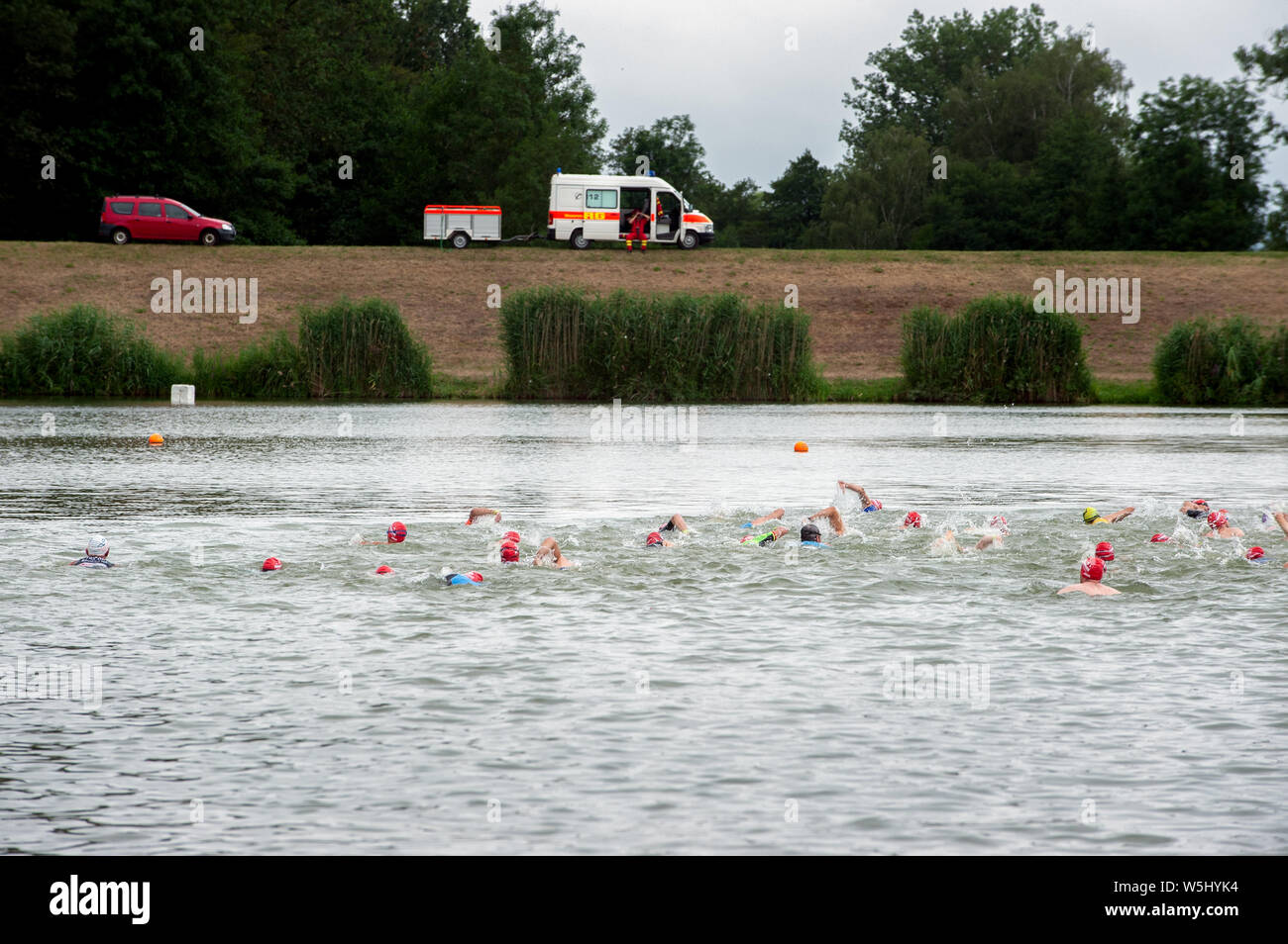 Degensbachsee, Germania, Luglio 2019: Triathlon Ilshofen. Gli atleti il nuoto nel lago e la vettura di soccorso con la supervisione di personale paramedico. Una profondità molto bassa Foto Stock
