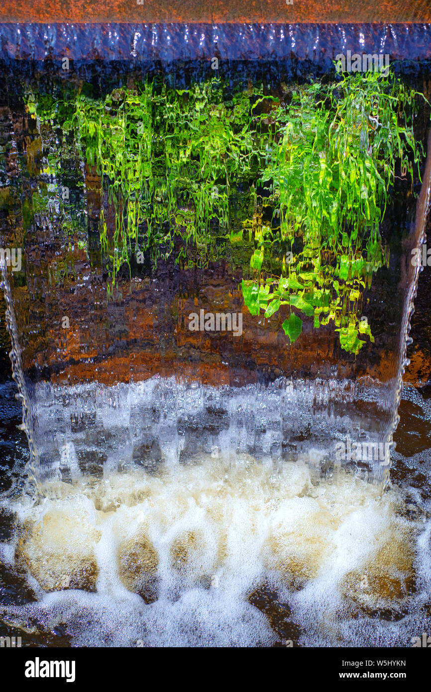 Cascata di acqua con spruzzi in un parco cittadino stagno e piante verdi in estate Foto Stock