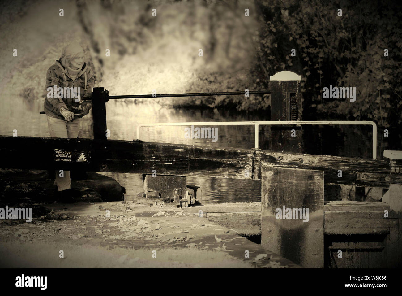 Fotografia in bianco e nero di donna apertura cancelli di blocco su British Waterways canal, mostrando una tonalità seppia immagine infrarossa, portando un datato e nostalgi Foto Stock