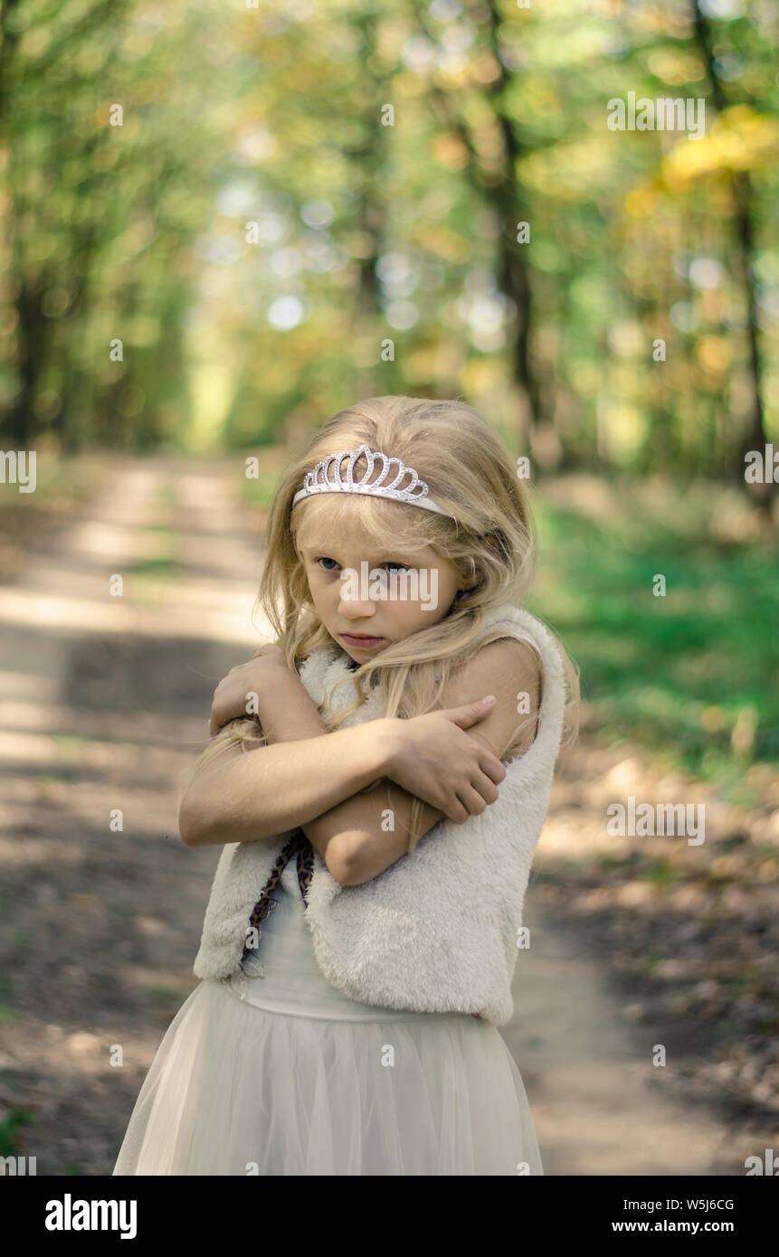 Una ragazzina in abito di congelamento in cammino tra alberi autunnali nella foresta in golden ora atmosfera Foto Stock