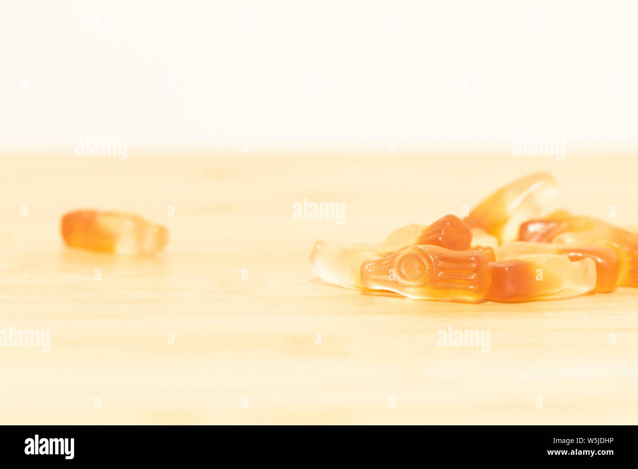 Molto leggero e sognante ritratto di alcuni cola a forma di bottiglia candy su un tavolo di legno. I dolci hanno gli stessi colori come una mezza bottiglia piena di cola. Foto Stock