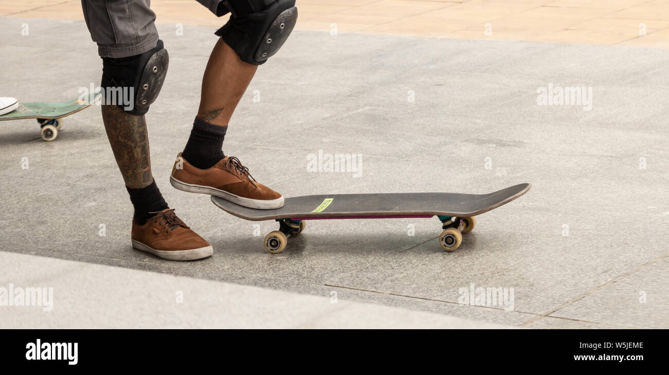 Tatuato guidatore di skateboard con ginocchiere in città skatepark. Foto Stock