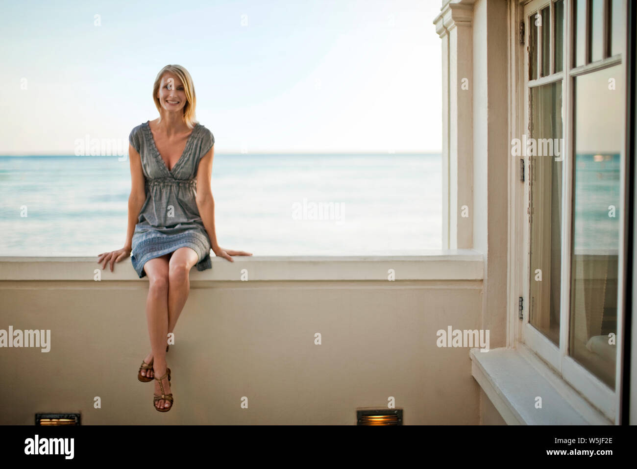 Metà donna adulta seduta sul davanzale della finestra della sua camera d'hotel. Foto Stock