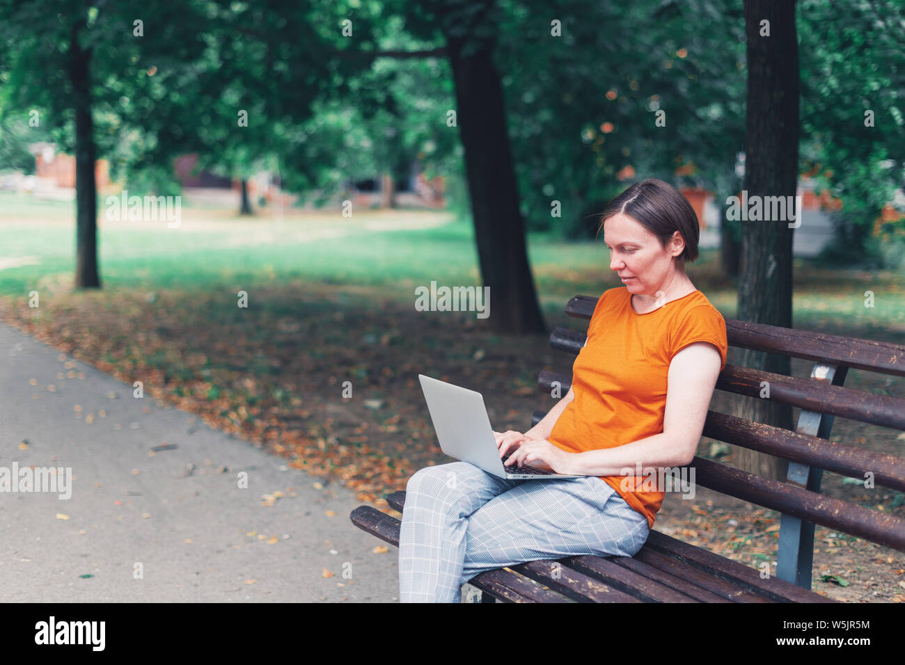 Donna che utilizza computer portatili sul banco di strada, mock up schermo. Adulto femmina caucasica blogger è la digitazione sulla tastiera, in qualsiasi luogo di lavoro lontano da casa off Foto Stock